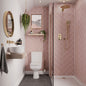 Multipanel Antique Rose Herringbone shower panels on display on all the walls with the gold shower head matching the pink wall panels with the toilet to the left-hand side of the shower with the shower panels behind it, and a mirror above the toilet with a little bit of storage - shower panels - The Wall Works